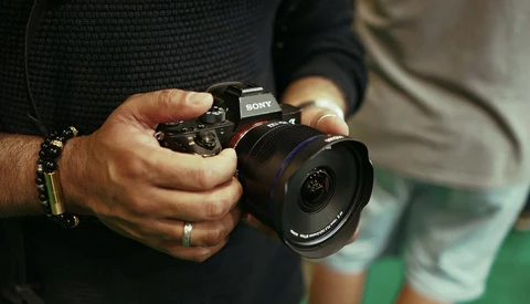 Photographer's hands holding a Sony mirrorless camera with wide-angle lens attached.