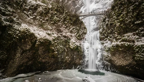 Frozen waterfall cascading between snow-covered canyon walls with a footbridge crossing above.