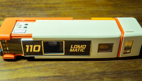 Lomo Matic 110 instant film camera with orange and white body on wooden surface.