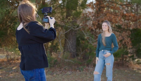 Photographer holding a smartphone on a tripod to photograph a subject outdoors.