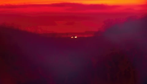 Silhouetted mountain ridges against a deep red and orange sunset sky with two distant lights visible on the horizon.