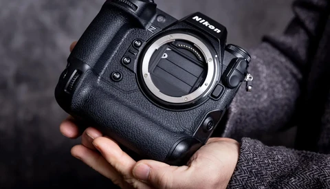 Nikon professional camera body held in hands, showing the lens mount and control buttons against a dark textured background.