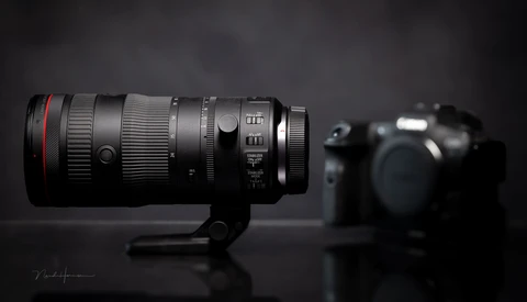 Professional telephoto lens with red ring mounted on stand, camera body blurred in background.