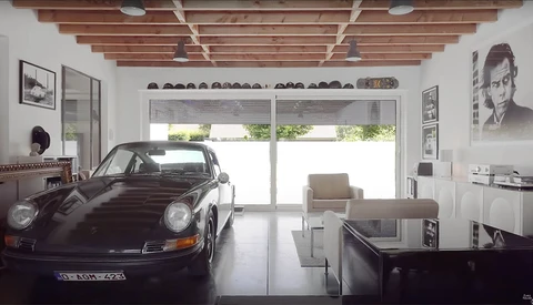 Black Porsche 911 displayed in a minimalist white garage with exposed wooden ceiling beams.