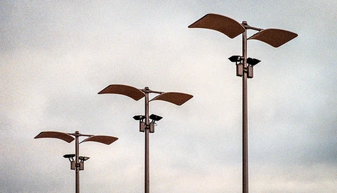 Three rusty metal wind vanes of increasing height arranged in a receding line against an overcast sky.