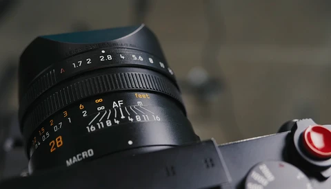 Close-up of a vintage manual focus lens showing aperture ring, focus scale, and macro marking.