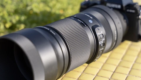 Telephoto lens mounted on a mirrorless camera body, positioned on a yellow surface outdoors.