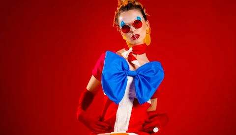 Person wearing red and white outfit with oversized blue bow against red background.