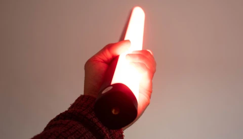 Hand holding a glowing white LED tube light against a neutral background.