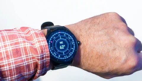 Smartwatch with blue digital display showing compass heading and temperature on wrist wearing red plaid shirt.