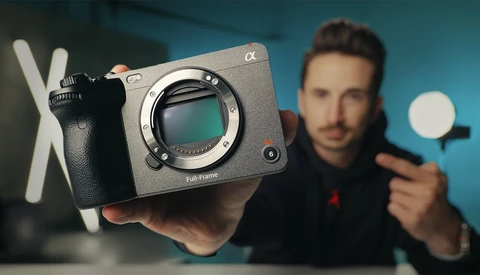 Photographer holding a mirrorless camera body with visible sensor and a ring light in studio setting.