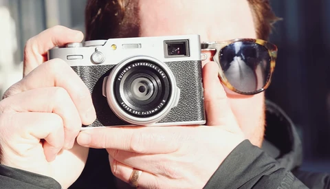 Person holding a rangefinder film camera with a fixed lens, wearing tortoiseshell sunglasses.