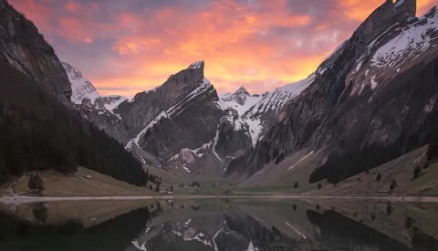 Alpine lake reflecting snow-capped mountains under a vibrant sunset sky.