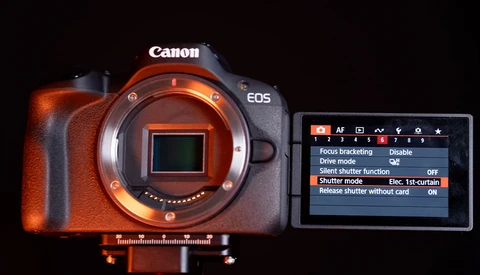 Canon EOS camera body with exposed sensor and rear LCD screen displaying menu settings.