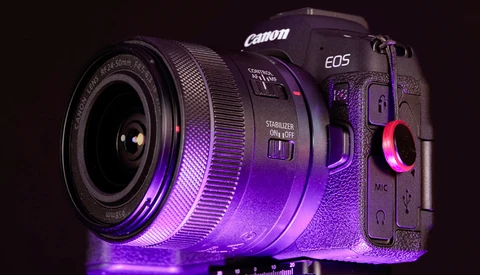 Canon EOS R5 mirrorless camera with attached lens, illuminated by purple and pink neon lighting against a dark background.