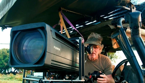 Cinematographer operating a large cinema camera mounted on a crane arm outdoors.