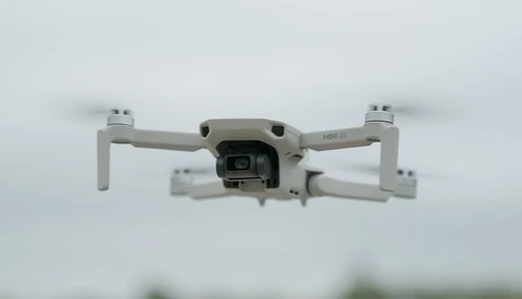 White compact drone photographed from below against an overcast sky.