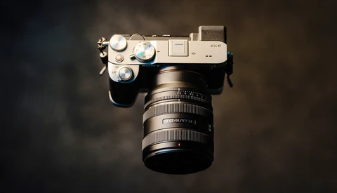 Overhead view of a silver mirrorless camera with attached zoom lens on dark background.