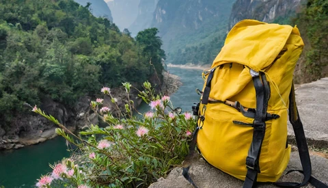 Bright yellow backpack resting on a rocky outcrop overlooking a misty mountain valley and river below.
