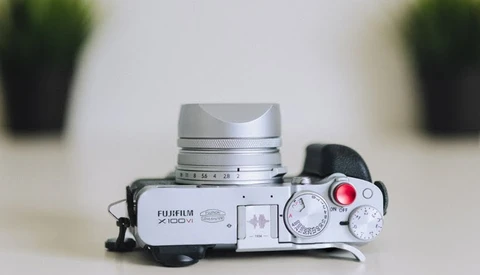 Silver Fujifilm X100VI rangefinder camera with lens cap and red shutter button visible on top.