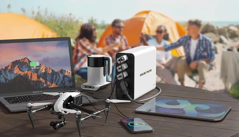 Photography and camping gear arranged on a wooden table with tents and campers visible in the background.