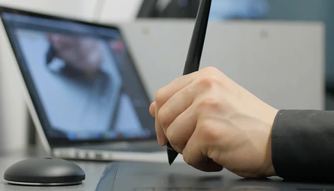 Person holding a stylus or pen tool while viewing an image on a laptop screen.