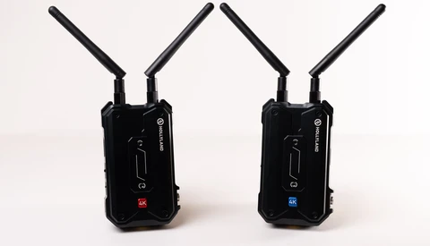 Two black wireless transmission units with dual antennas positioned side by side against a white background.