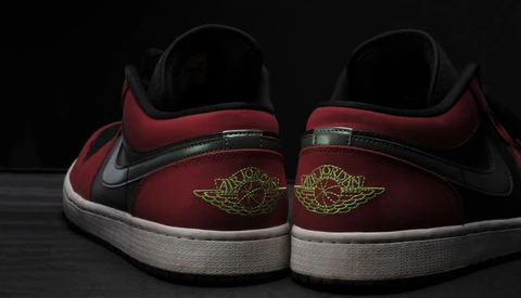 Rear view of red and black sneakers with white sole and gold wing logo embroidery.