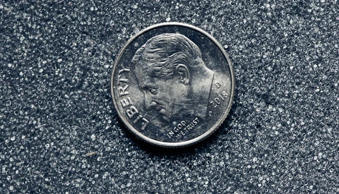 Close-up of a silver coin with a profile portrait facing left on a textured gray surface.