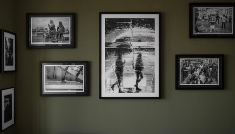 Gallery wall with seven black-framed black and white photographs arranged on olive-green wall.
