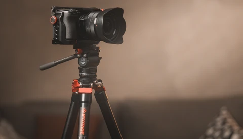 Professional cinema camera mounted on tripod with fluid head and extended lens hood.