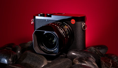 Leica rangefinder camera with mounted lens on dark rocks against deep red background.