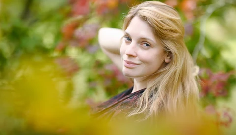 Young woman with long blonde hair looking over her shoulder in an outdoor garden setting.