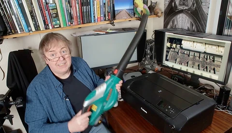 Person holding a turquoise camera at a desk setup with monitors and photography equipment.
