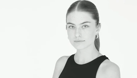 Portrait of a woman with pulled-back hair wearing a black sleeveless top against a white background.