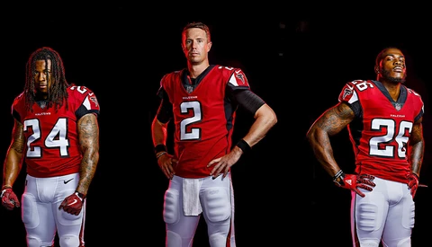 Three football players in red jerseys posed against black background.
