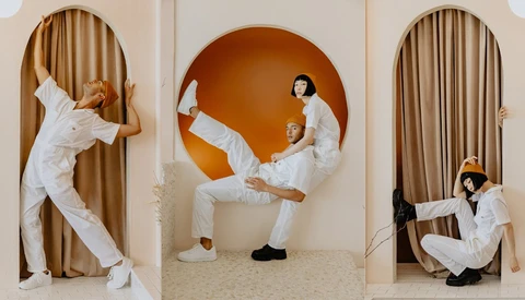 Three people in white clothing posing dynamically in arched doorways with tan curtains and an orange circular backdrop.