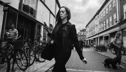Woman in dark jacket walking down a European cobblestone street lined with bicycles and period buildings.