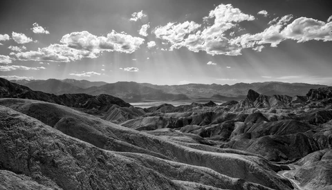 Dramatic black and white landscape of deeply eroded badlands with layered terrain under a cloudy sky.