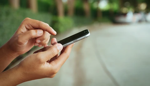 Hands holding a smartphone outdoors with blurred green foliage in the background.