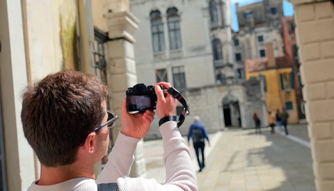 Photographer holding a camera at arm's length to frame a historic European plaza with classical architecture.