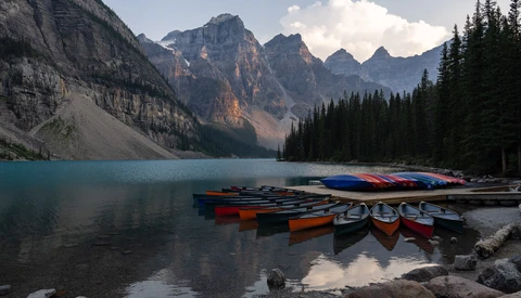 Colorful rental canoes lined up on a turquoise alpine lake shoreline beneath dramatic mountain peaks.