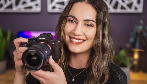 Woman holding a Sony mirrorless camera with a wide-angle lens in a studio setting.