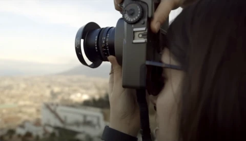 Photographer holding a vintage film camera with telephoto lens, capturing an aerial cityscape view.