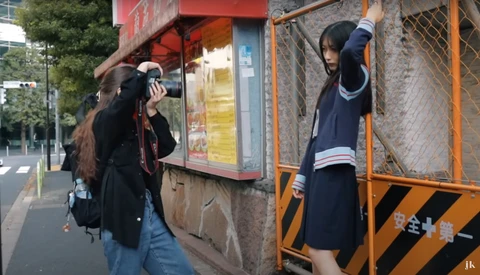 Two students in school uniforms posing playfully against urban storefronts and metal structures.