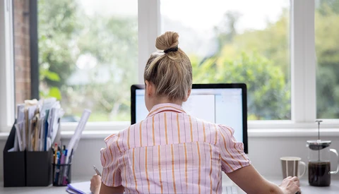 Woman working at desktop computer near bright windows with natural outdoor light streaming in.