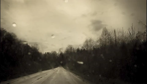 Straight road stretching into distance under overcast sky with bare trees flanking both sides.