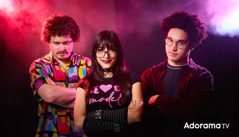 Three people posing against a pink and purple gradient backdrop with dramatic colored lighting.