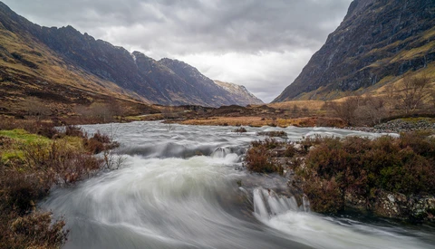 Mountain river flowing through a valley with dramatic peaks and overcast sky.