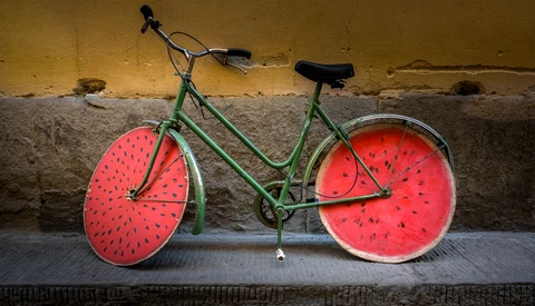 Green bicycle with watermelon-designed wheels leaned against a weathered yellow and gray wall.